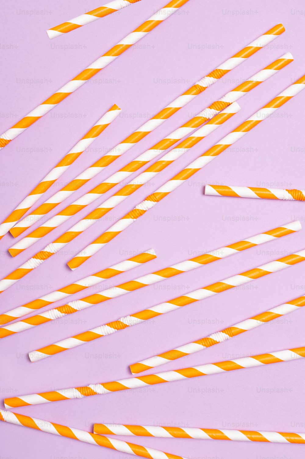 Pajitas de papel a rayas naranjas y blancas sobre un fondo púrpura