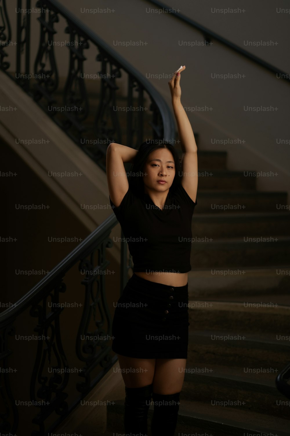 a woman in a black top and skirt standing in front of a stair case