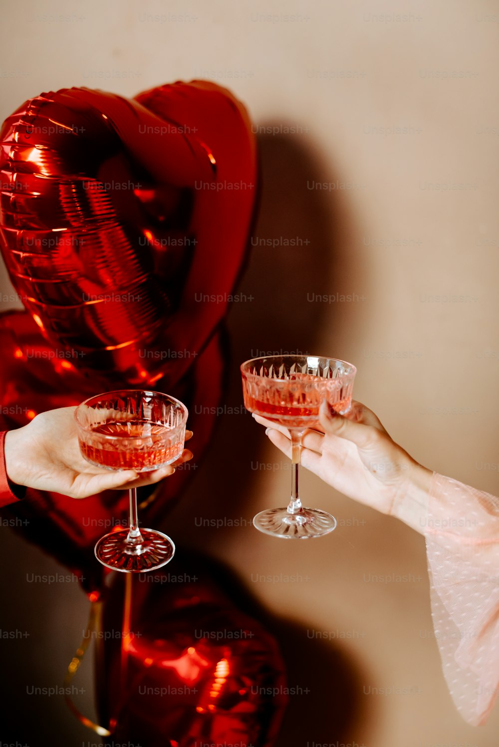 a person holding two glasses of wine in front of balloons