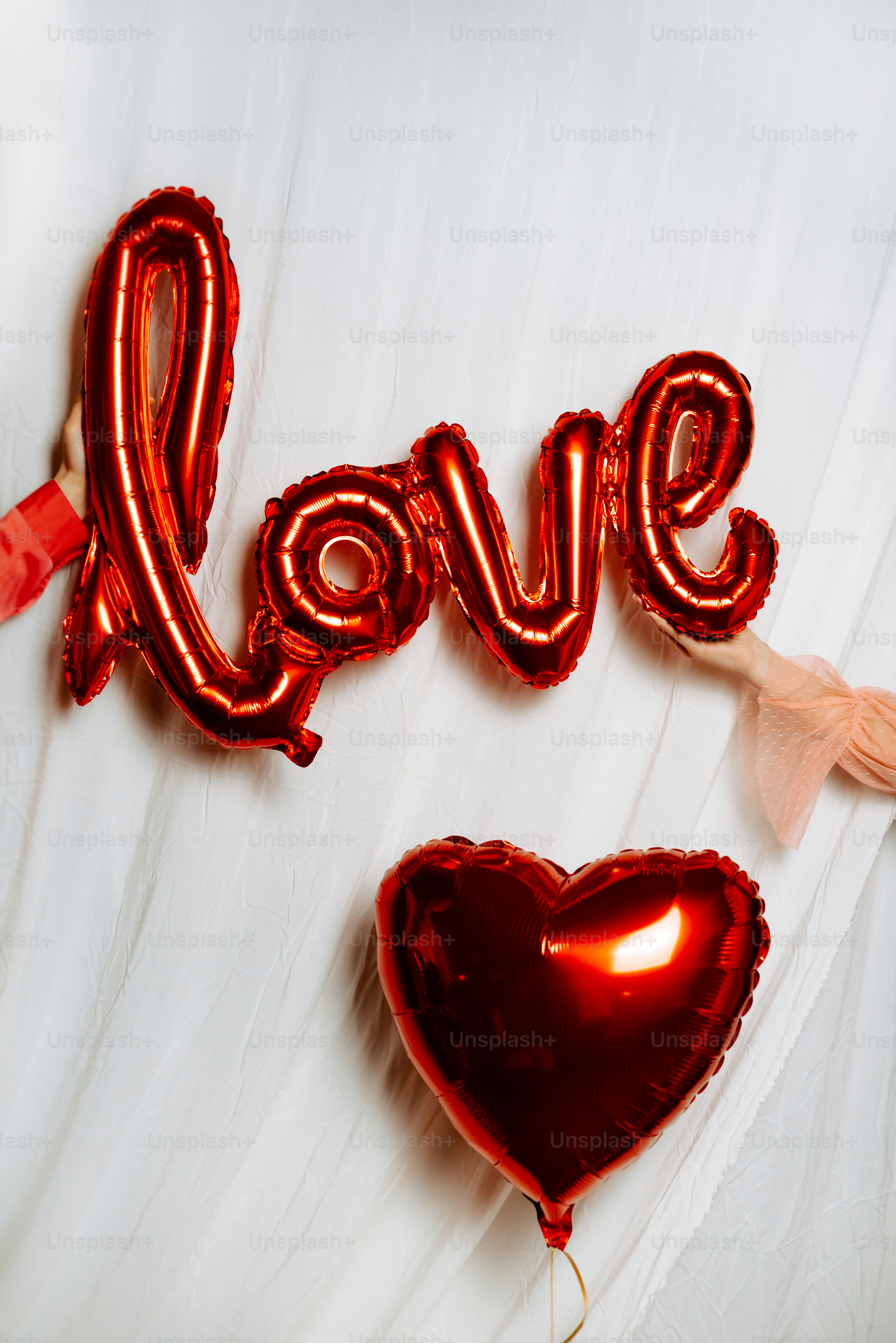 a couple of red heart shaped balloons sitting on top of a bed