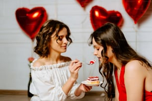 Dos mujeres están comiendo pastel juntas frente a globos en forma de corazón