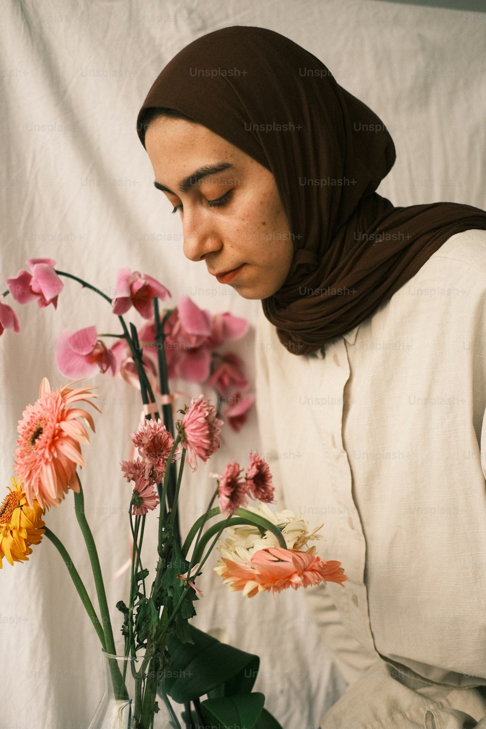 a woman in a headscarf arranging flowers in a vase