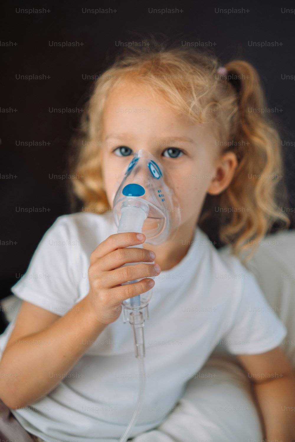 a little girl in a white shirt is holding an oxygen tube