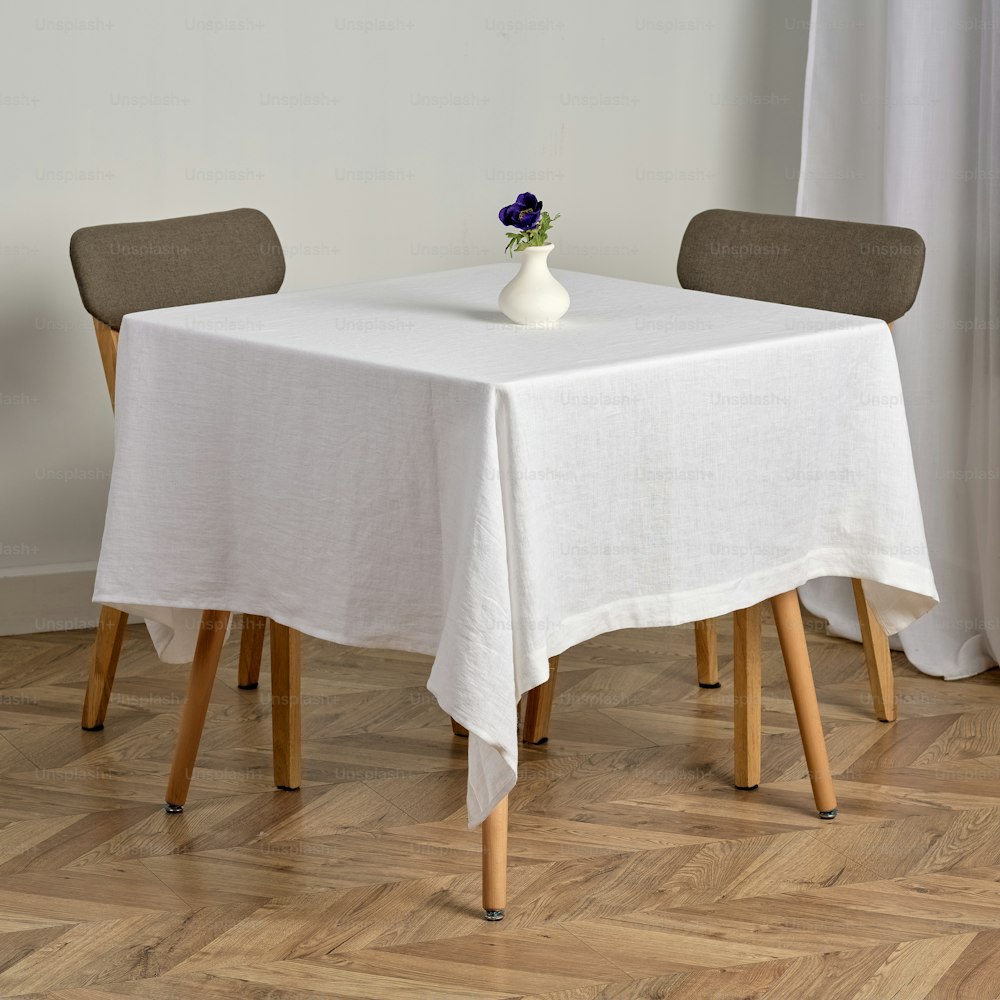 una mesa blanca con dos sillas y un jarrón con una flor