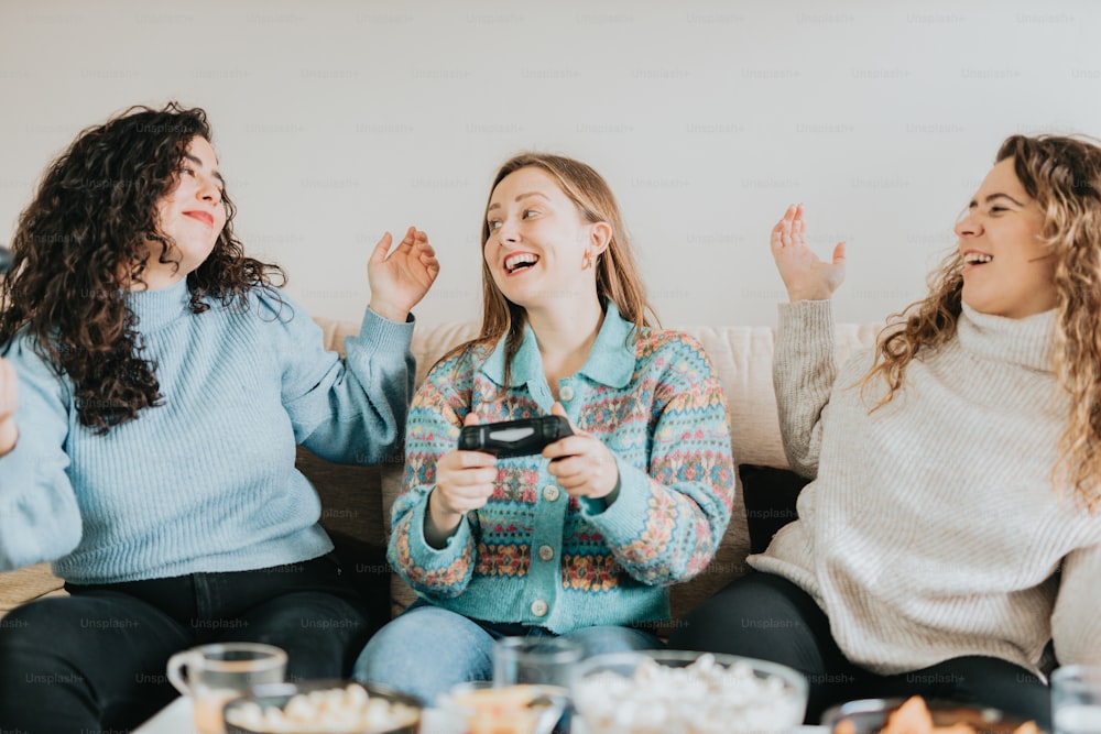 three women sitting on a couch laughing and playing a video game