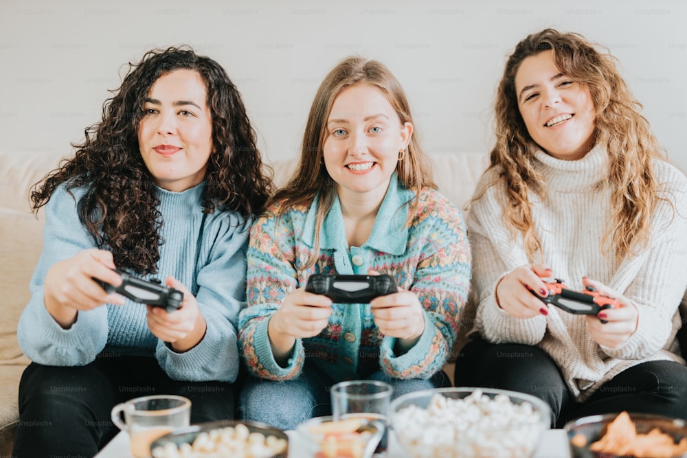 Drei Frauen sitzen auf einer Couch und spielen Videospiele