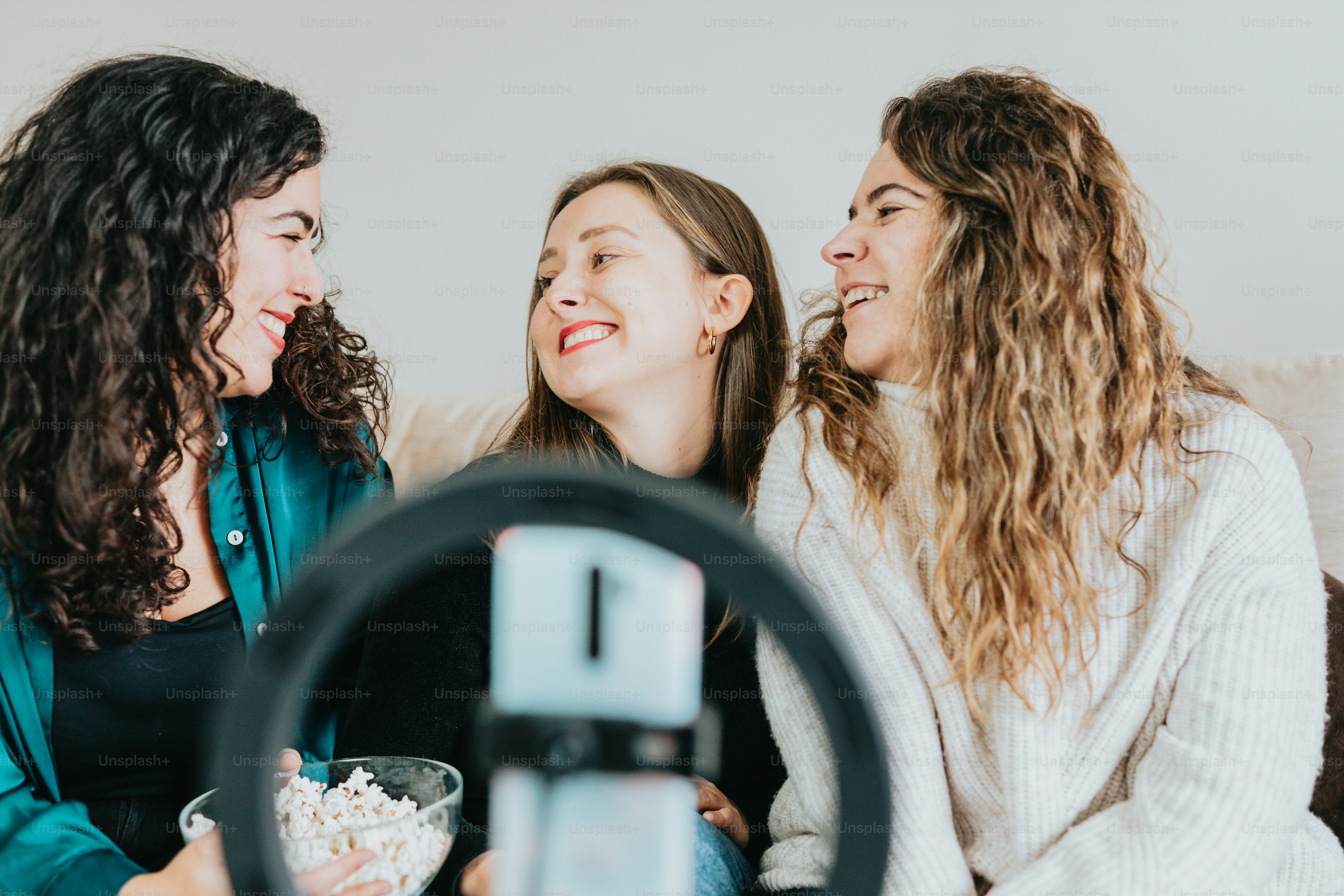 three women sitting on a couch with a bowl of popcorn