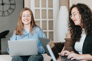 two women sitting on a bed with laptops