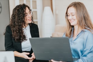 two women sitting on a couch looking at a laptop