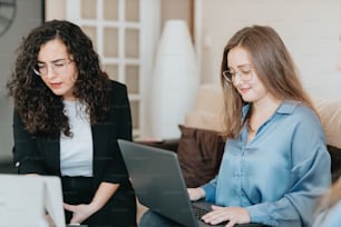 two women sitting on a couch looking at a laptop