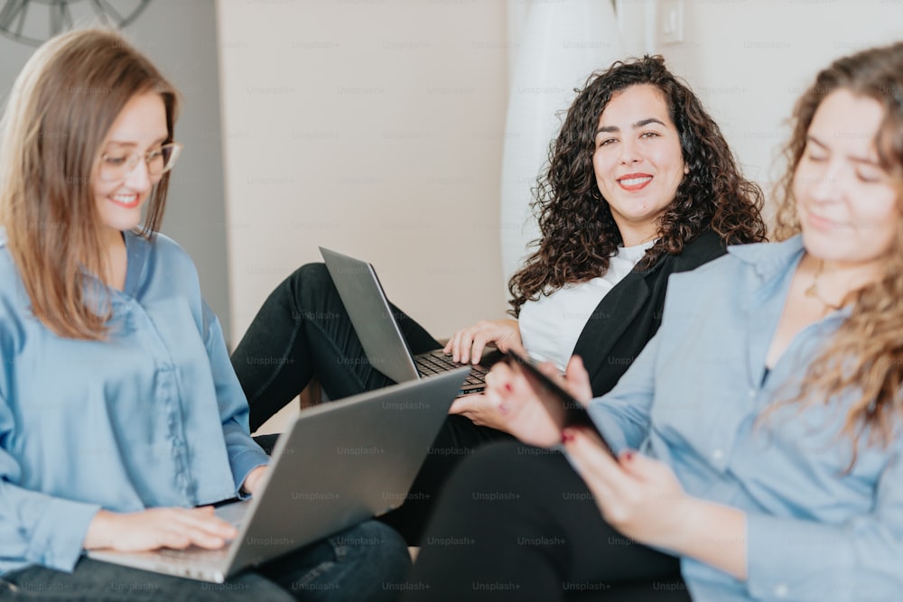 two women sitting on a couch using laptops