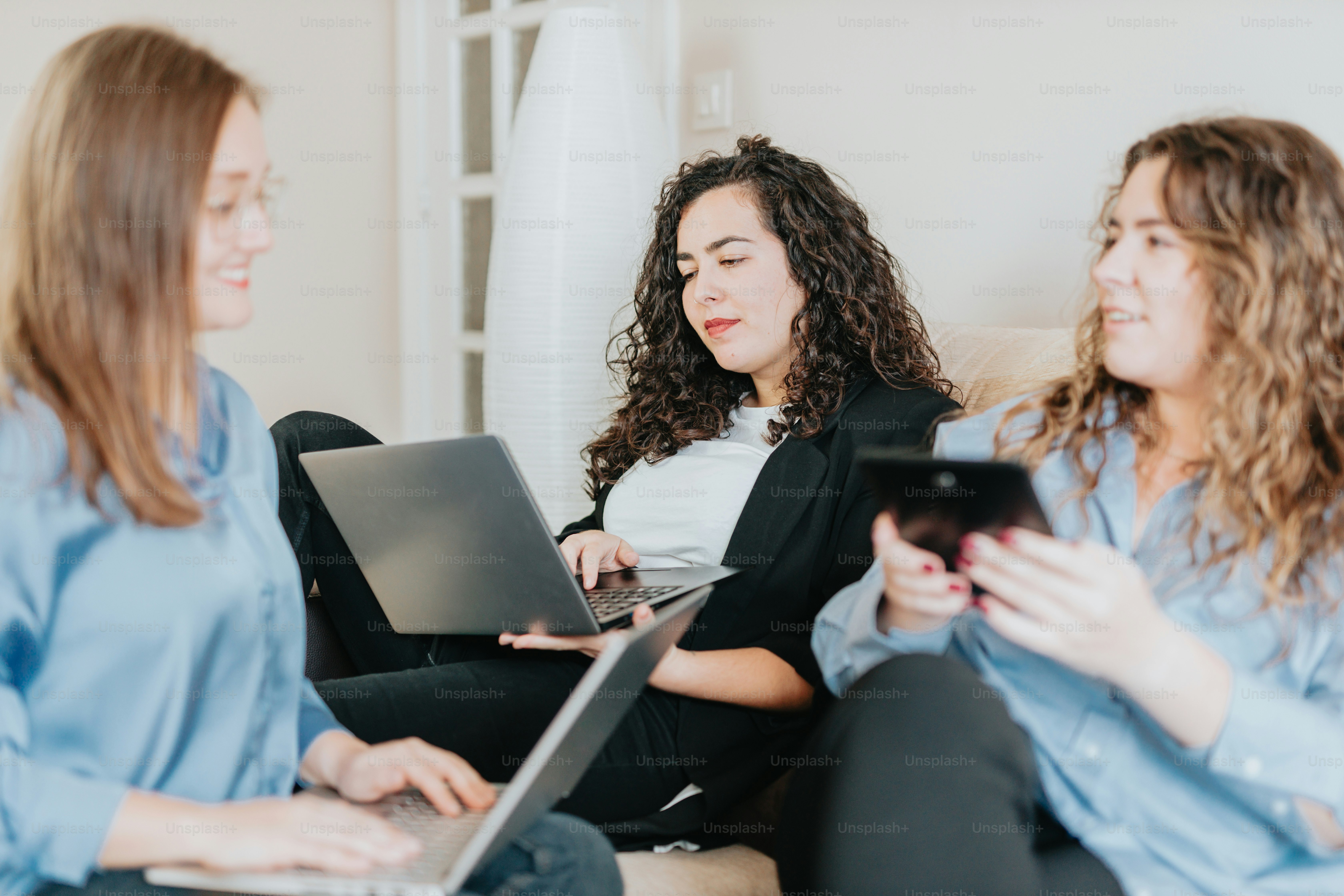 three women sitting on a couch looking at their laptops