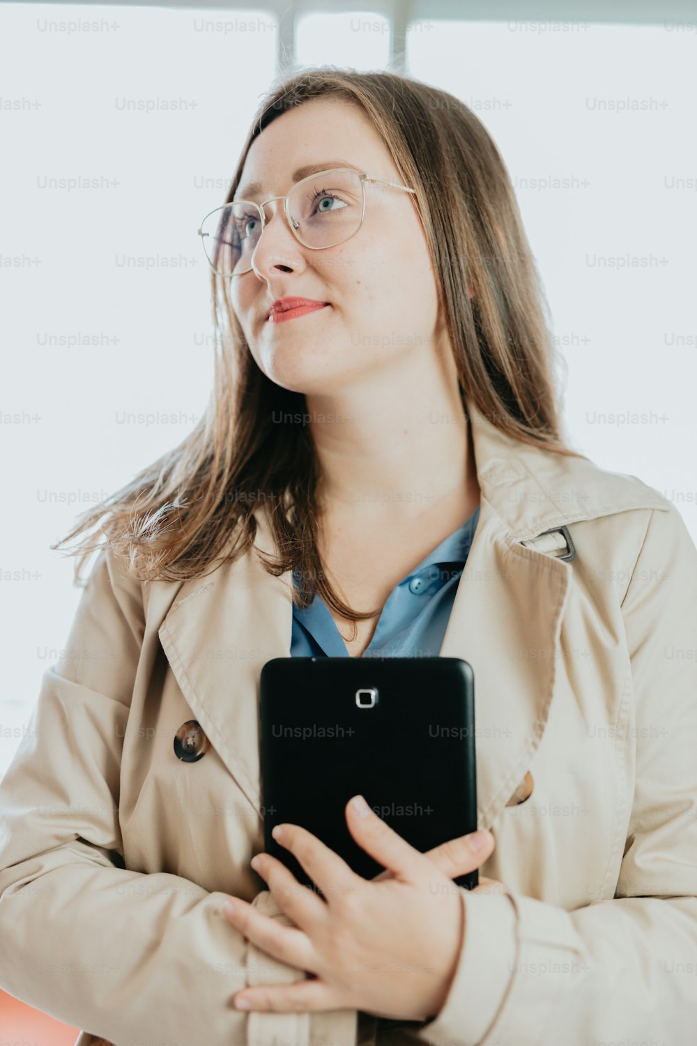 a woman in a trench coat holding a tablet