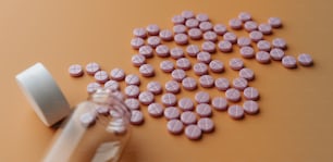 Una bottiglia piena di pillole rosa accanto a una pila di pillole rosa