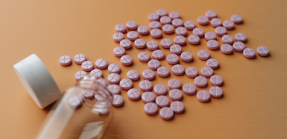 une bouteille remplie de pilules roses à côté d’une pile de pilules roses