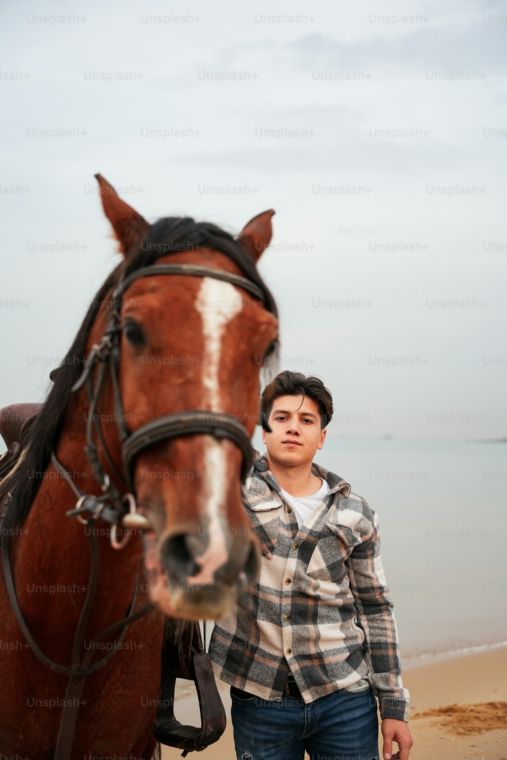 a man standing next to a horse on a beach