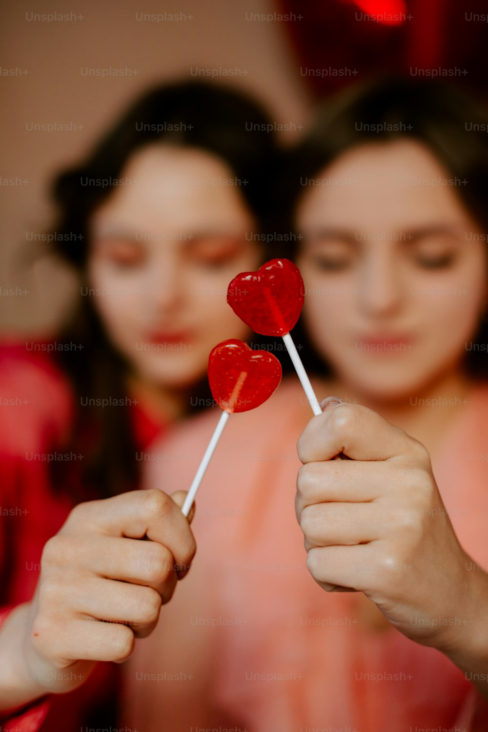 a couple of women holding up two heart shaped lollipops