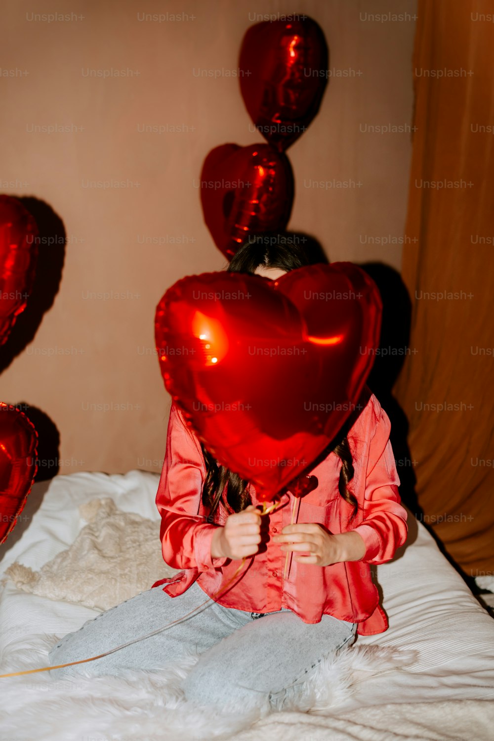 a little girl sitting on a bed holding a heart shaped balloon