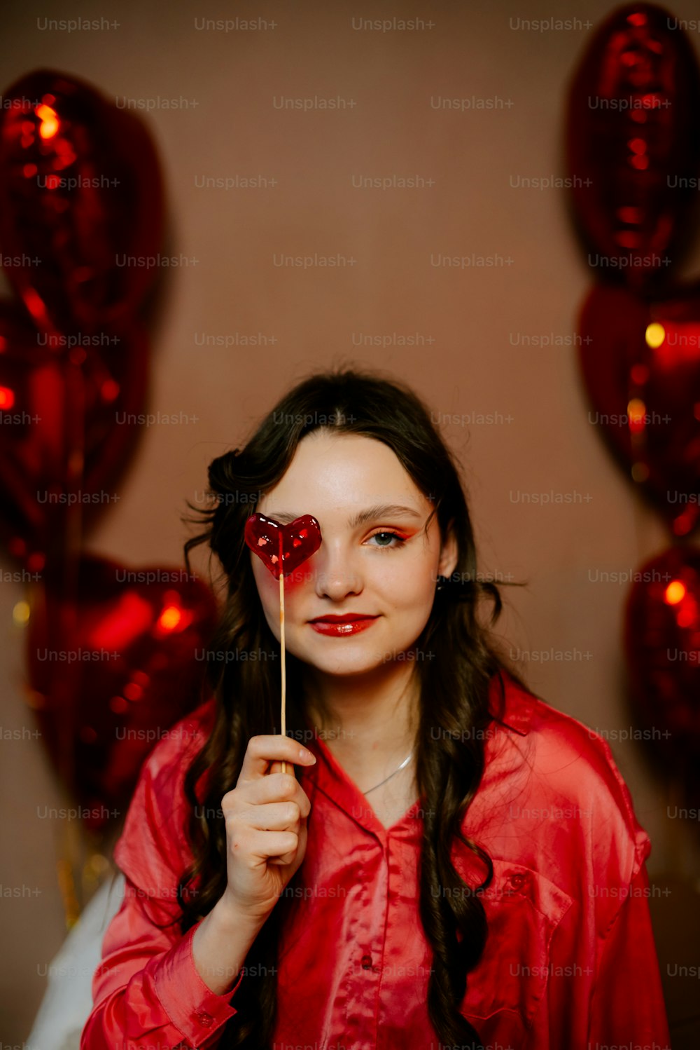 a woman holding a heart shaped lollipop in front of her face