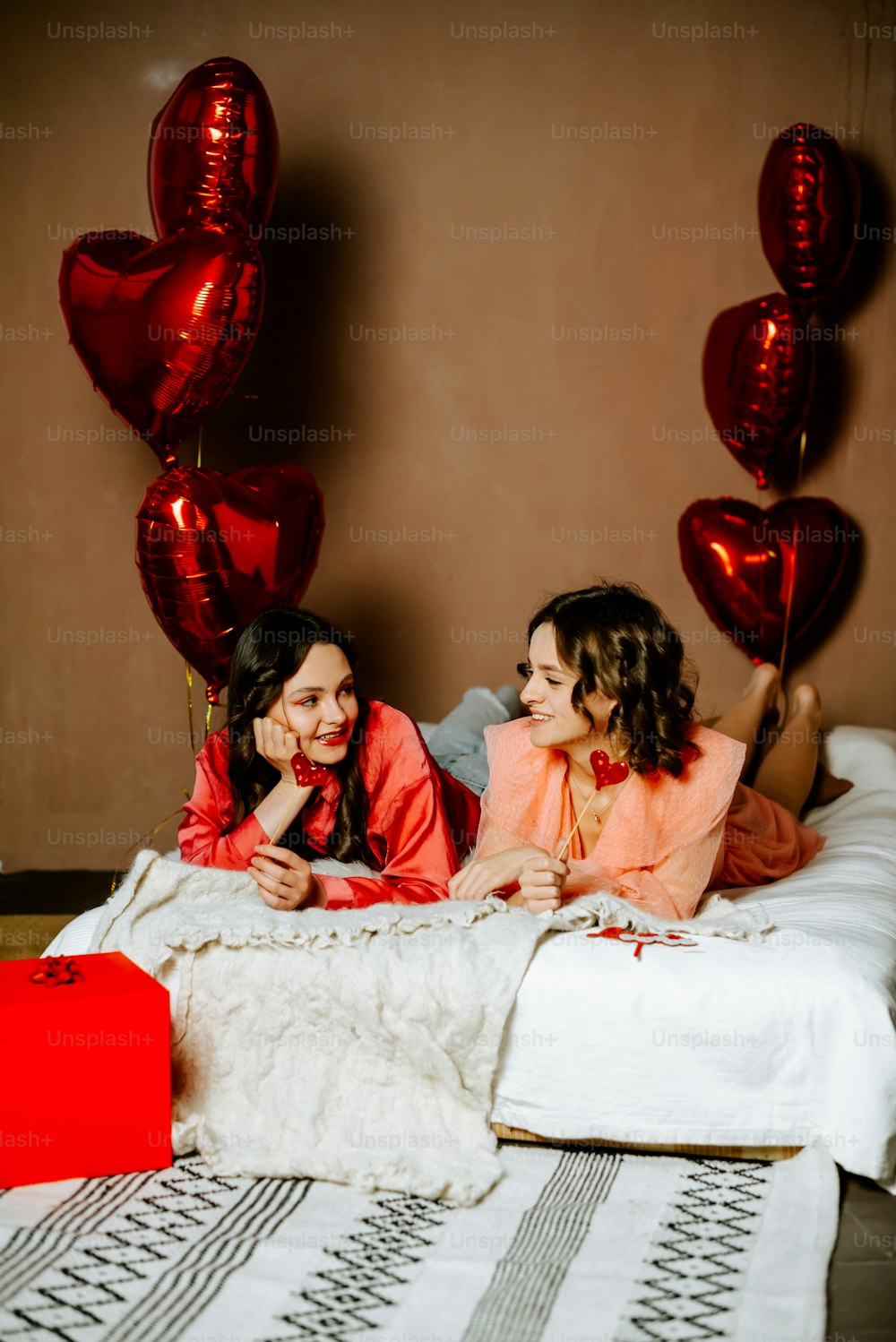 two women laying on a bed with red balloons