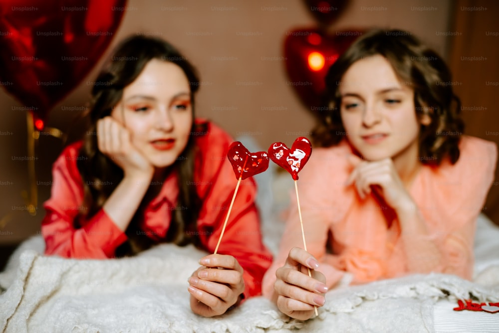 a couple of girls laying in bed with a heart shaped lollipop