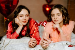 a couple of girls laying in bed with a heart shaped lollipop