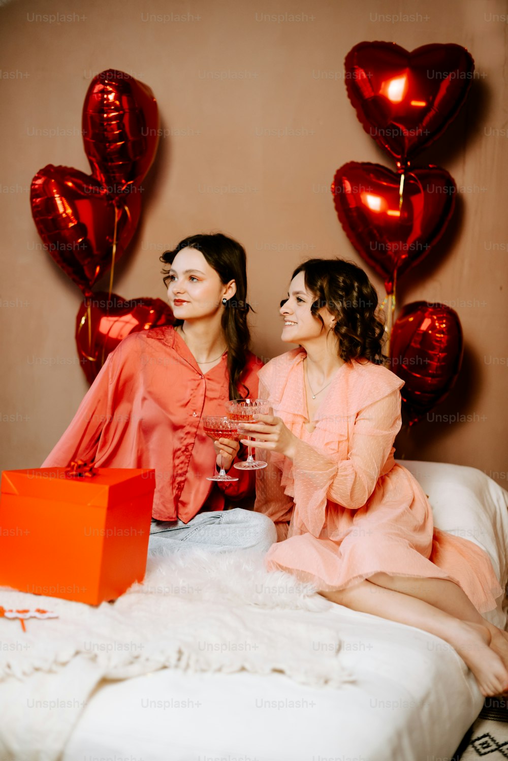 two women sitting on a bed holding wine glasses