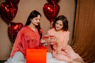 two women sitting on a bed holding wine glasses