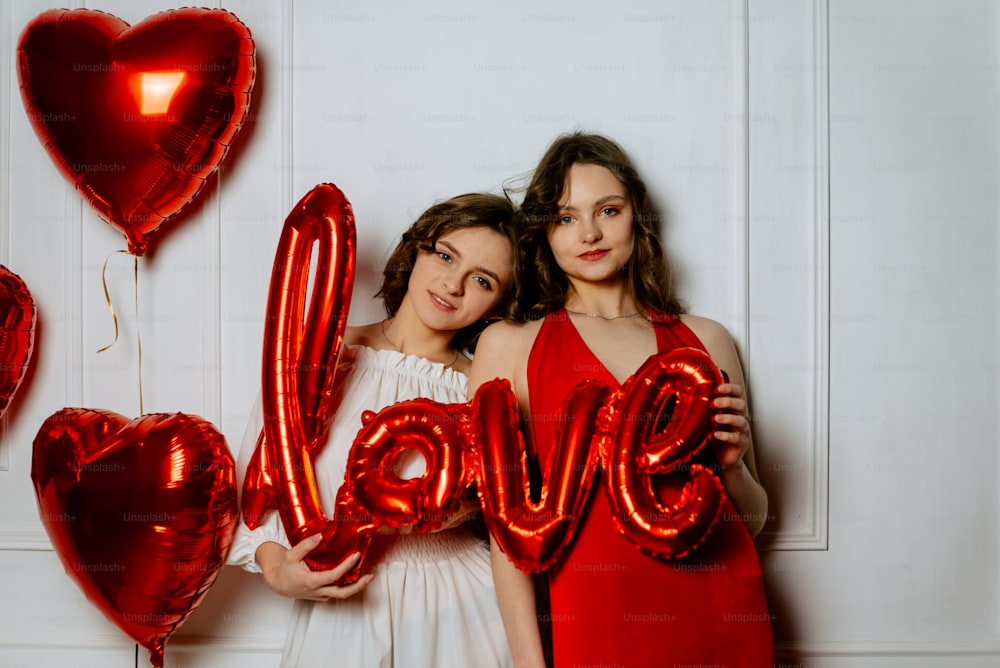 two girls holding red balloons that spell out the word love