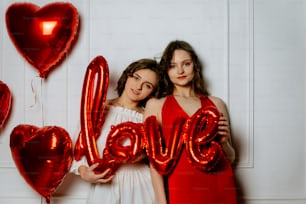 two girls holding red balloons that spell out the word love