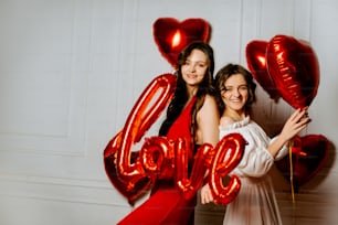 two girls are posing for a picture with balloons in the shape of the word love