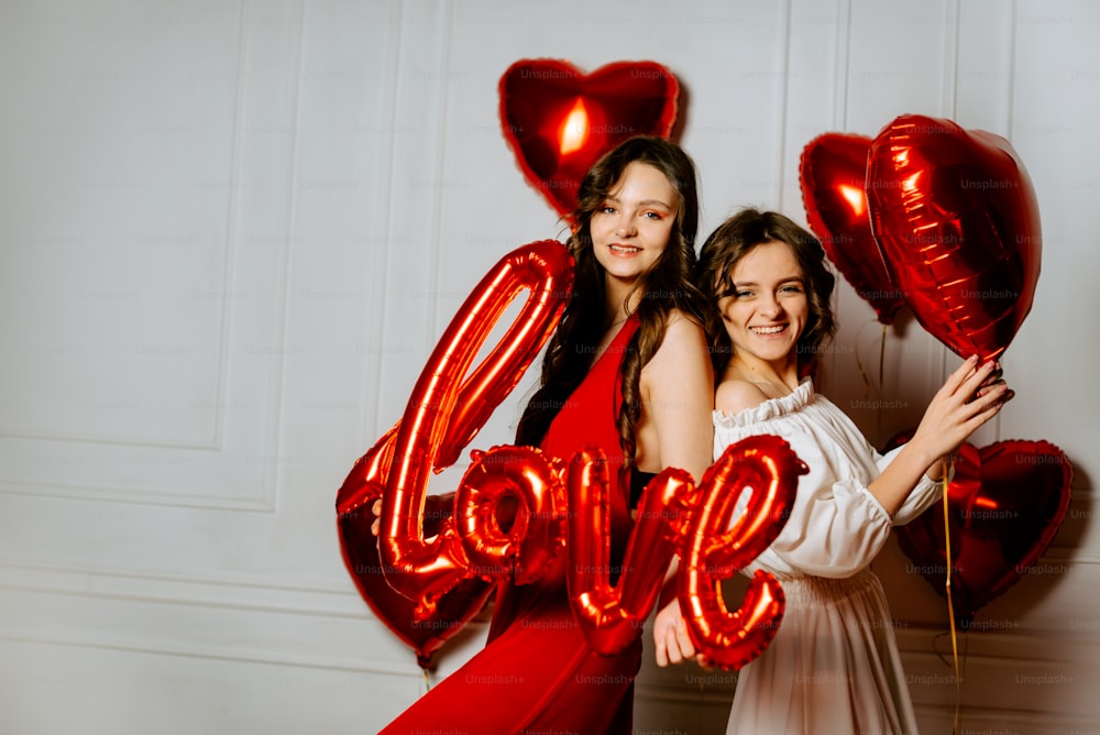 two girls are posing for a picture with balloons in the shape of the word love