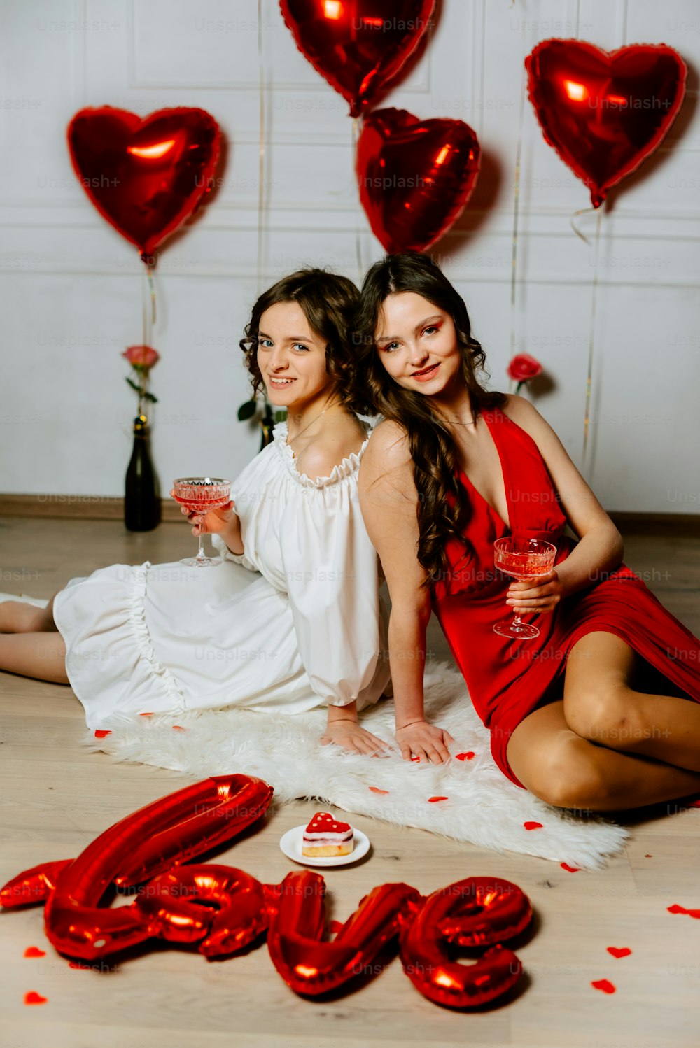 two women sitting on the floor with red balloons