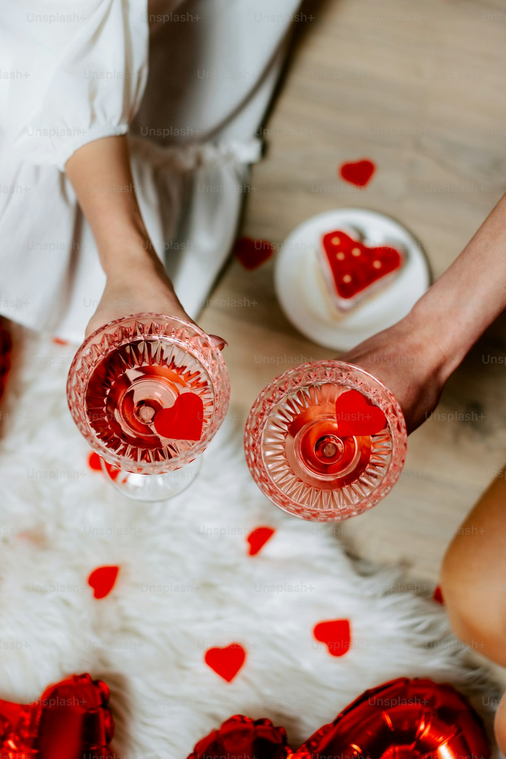 two people holding glasses with red liquid in them