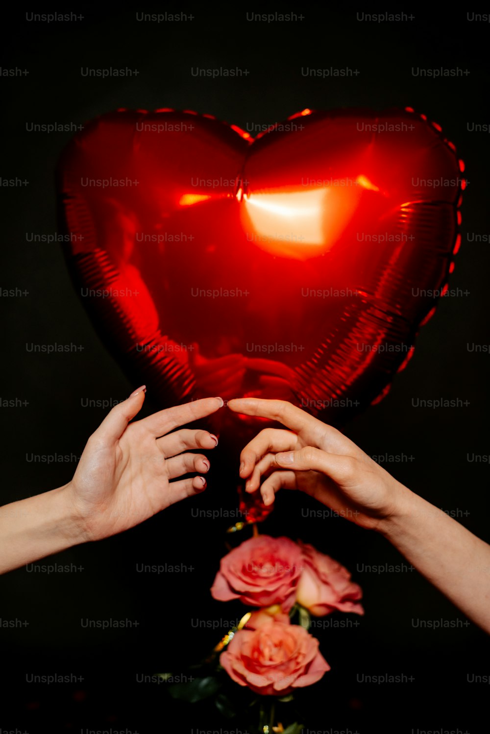 two hands reaching for a heart shaped balloon