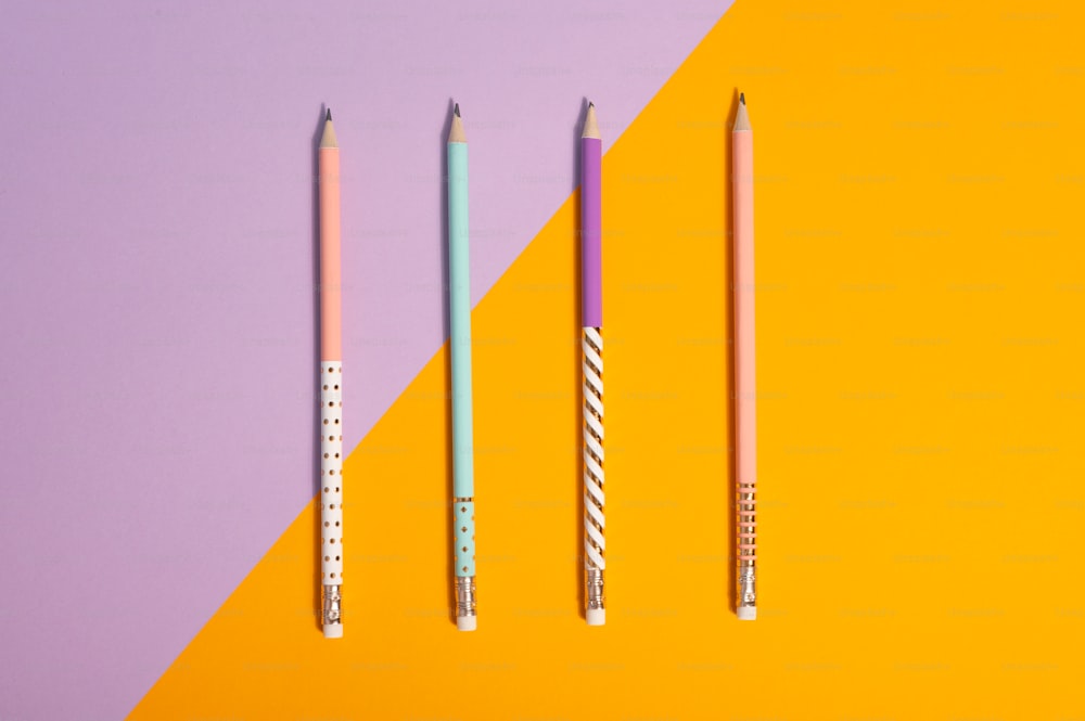 黄色と紫の背景に3本の鉛筆が並ぶ