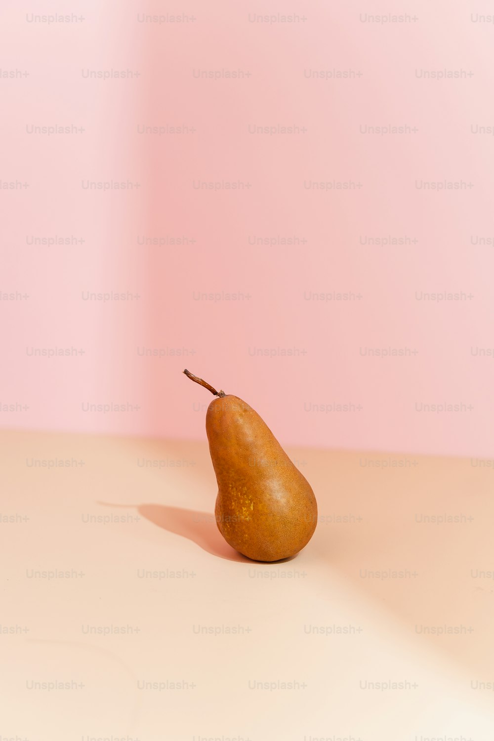 Una sola pera sentada en una mesa frente a una pared rosa