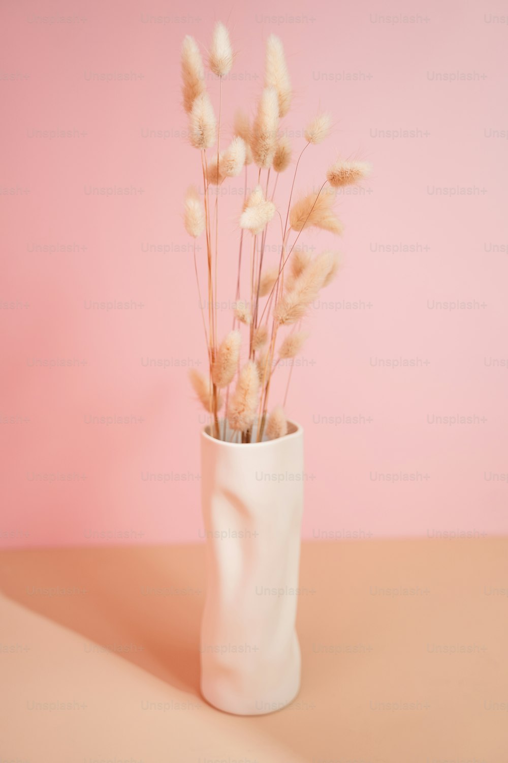 a white vase filled with dry grass on top of a table