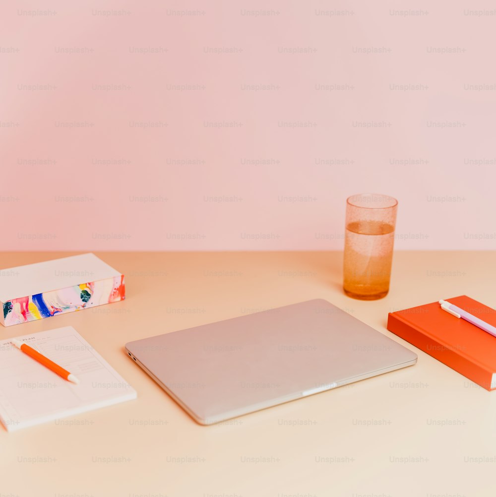 una scrivania con un computer portatile, un notebook e un bicchiere di succo d'arancia