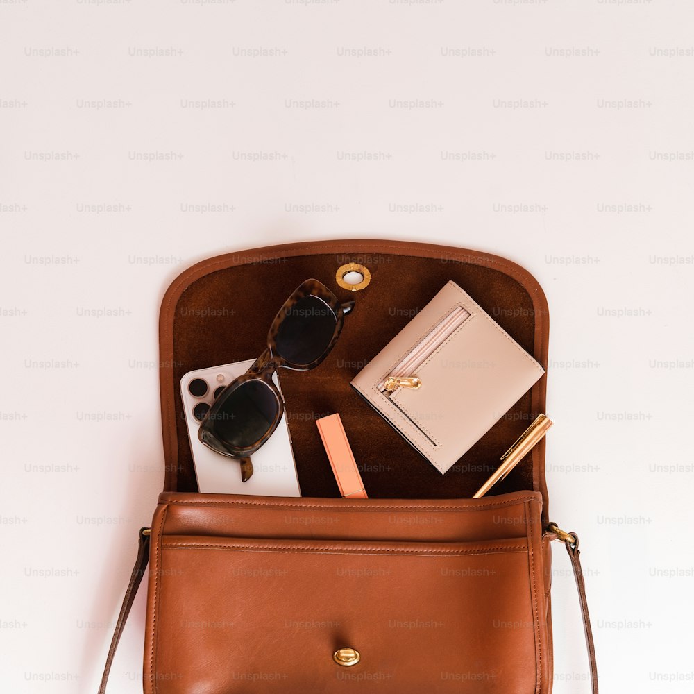 un sac à main marron avec une paire de lunettes de soleil et un cahier