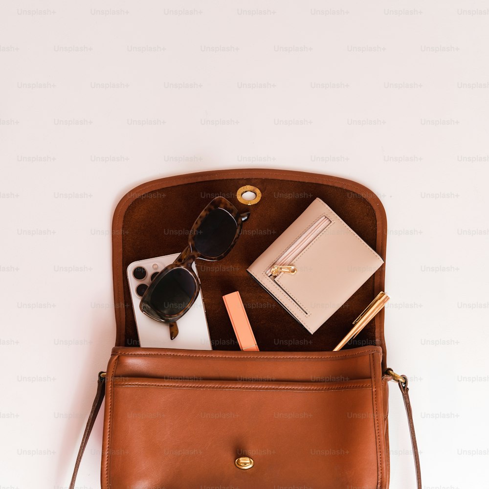 eine braune Handtasche mit einer Sonnenbrille und einem Notizbuch