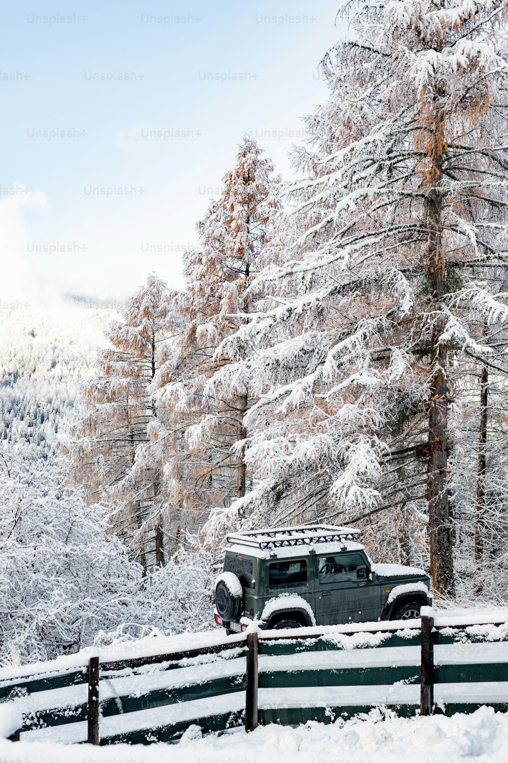 a jeep is parked in the snow near a fence