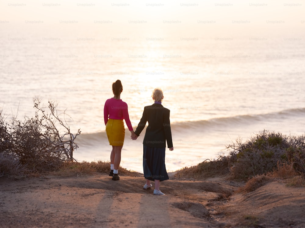 a couple of women walking down a dirt road next to the ocean