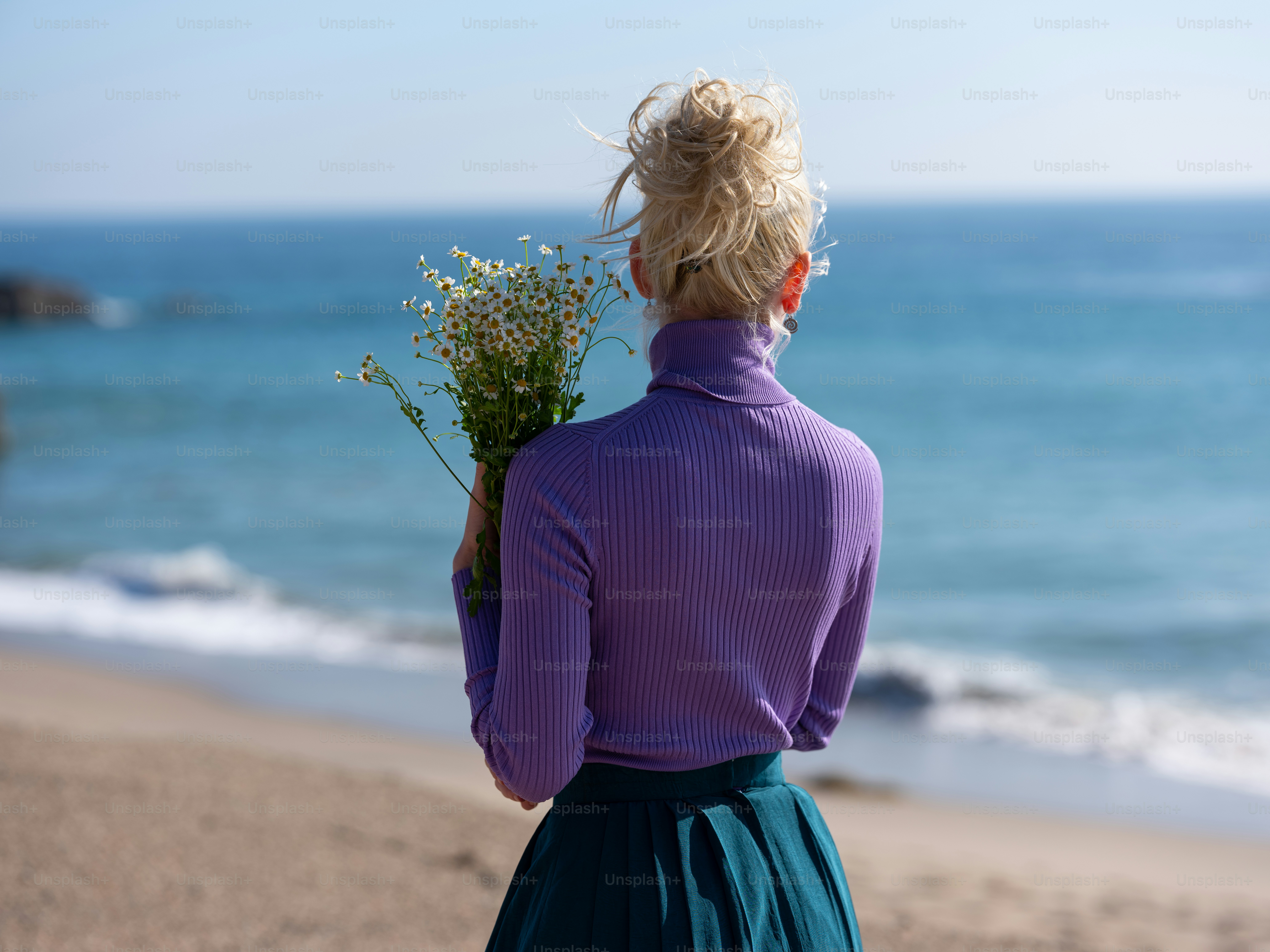 Una mujer parada en una playa sosteniendo un ramo de flores