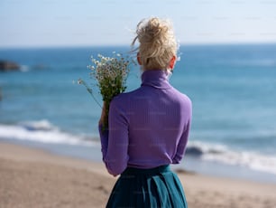 uma mulher em pé em uma praia segurando um buquê de flores