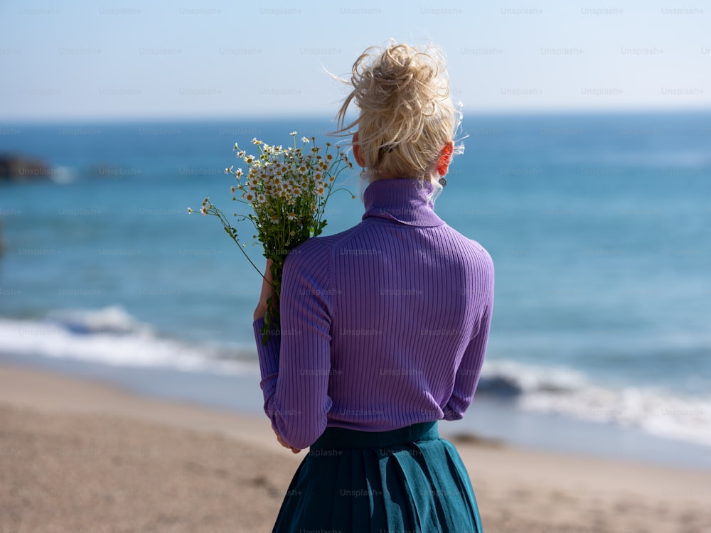 Una mujer parada en una playa sosteniendo un ramo de flores