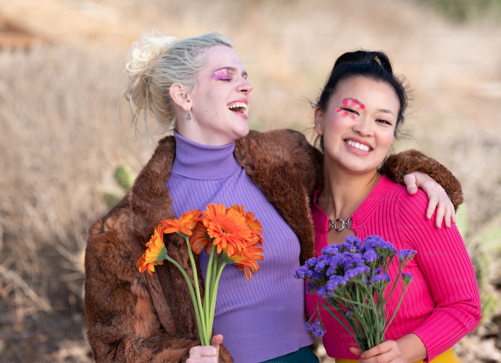 um casal de mulheres de pé um ao lado do outro segurando flores