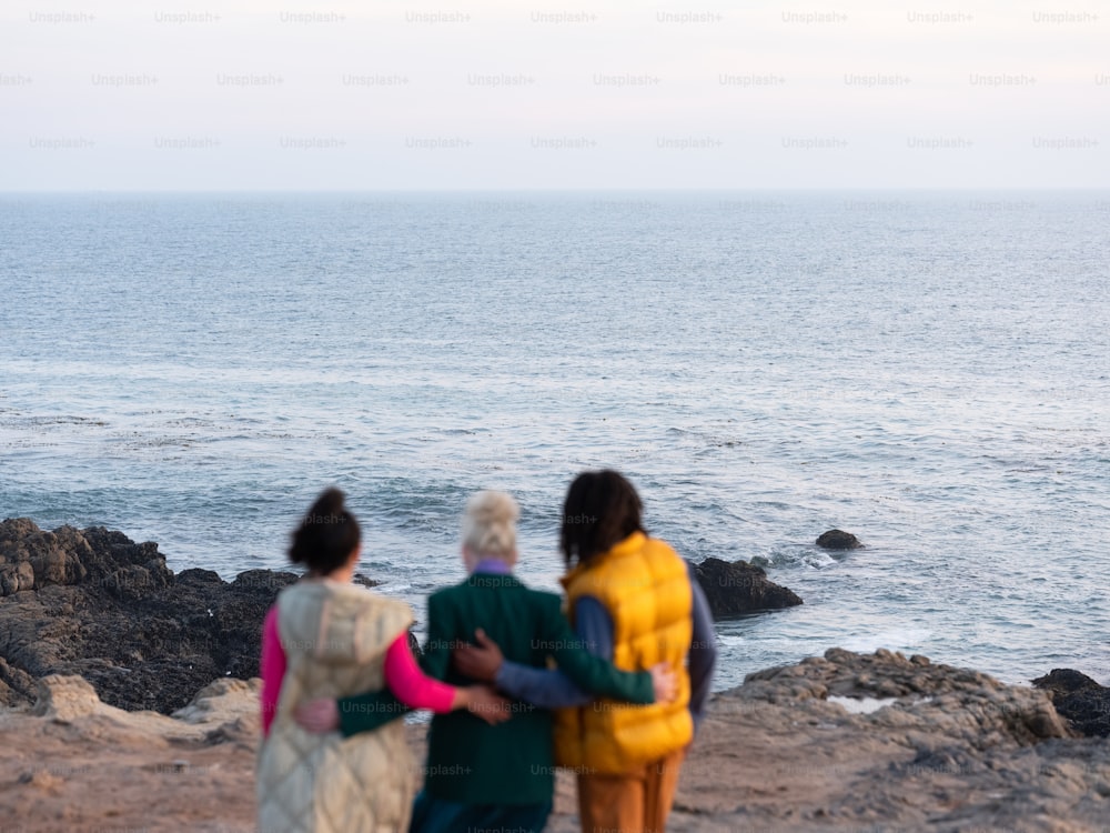 Drei Frauen stehen an einem felsigen Strand und blicken auf den Ozean