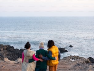 岩だらけのビーチに立って海を眺める3人の女性