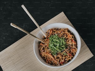 a bowl of noodles with vegetables and chopsticks
